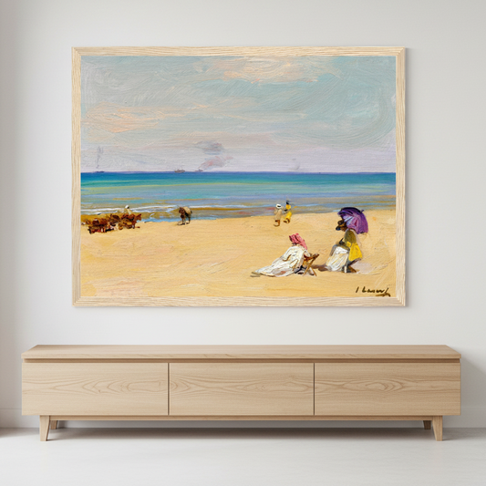 A framed beach painting hanging on a white wall above a light wood console table. The artwork depicts a sandy beach, blue ocean, and a few small figures under a pale sky.