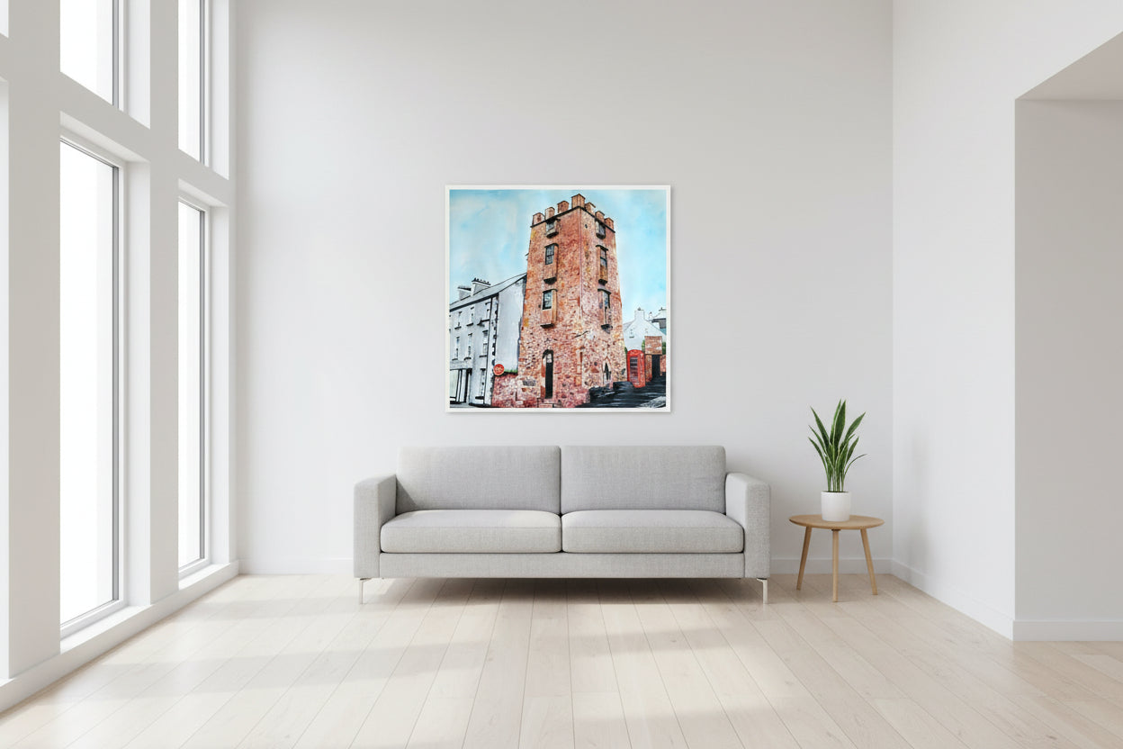 70×70 cm white-framed art print of The Curfew Tower Cushendall in a bright, modern open-plan interior, clean wall space, minimalist furniture, daylight through large windows, luxury home décor photography by Artist Ó Maoláin. This piece depicts The Curfew Tower in Cushendall, Glens of Antrim, built by Francis Turnley in 1820 and now owned by Bill Drummond. The artwork showcases the tower amid the scenic Glens of Antrim.