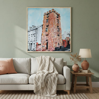 Large 70×70 cm natural oak-framed art print of The Curfew Tower Cushendall displayed in a warm Irish-inspired home interior, muted earthy palette, soft lamplight ambience, premium lifestyle photography highlighting frame texture and artwork detail.”Framed art print 'The Curfew Tower' by Ó Maoláin. This piece depicts The Curfew Tower in Cushendall, Glens of Antrim, built by Francis Turnley in 1820 and now owned by Bill Drummond. The artwork showcases the tower amid the scenic Glens of Antrim.
