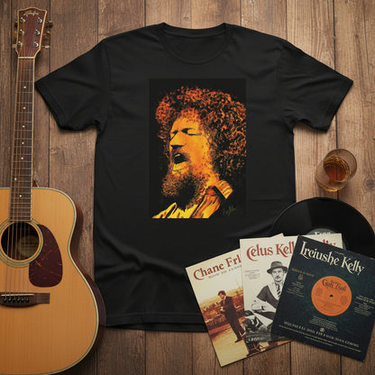 Luke Kelly T-shirt laid flat beside acoustic guitar, whiskey glass, and Irish vinyl records. Warm indoor light, cultural storytelling style.