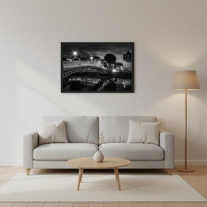 Black and white framed wall art print of Dublin's iconic Ha'penny Bridge at night. The detailed photograph captures the bridge's intricate architecture and its reflection in the River Liffey, creating a timeless and elegant piece perfect for home or office decor Minimalist living room, neutral walls, Ha’penny Bridge black and white framed print, 30x45 cm, black wooden frame, hanging above a light grey sofa, soft evening lamp light, Scandinavian decor,