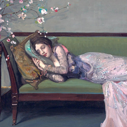 Woman in a pink dress lying on a green couch with flowers in her hair, in a room with a gray wall.