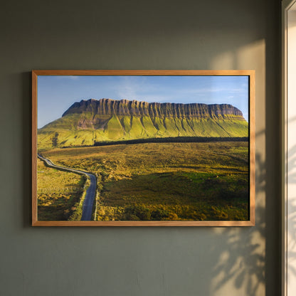 Benbulben, Sligo framed print in a natural oak frame on a dark green wall beside a window, dappled plant shadow