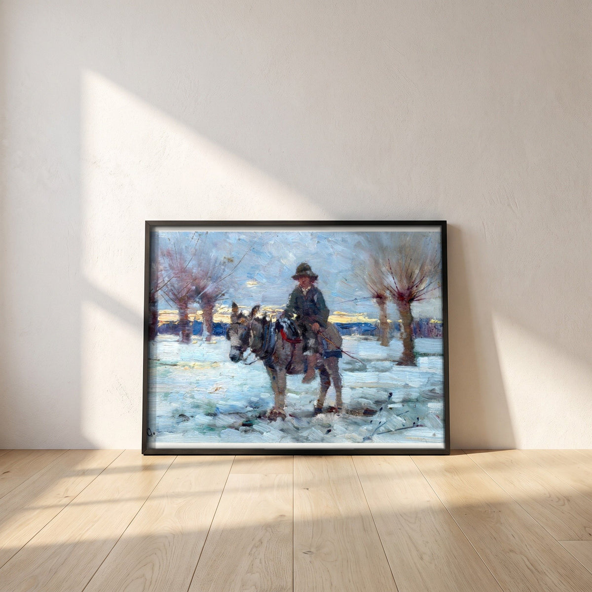 Boy on a Donkey in a Snowy Landscape by Walter Osborne framed print in a black frame leaning against a white plaster wall on oak floorboards in morning light