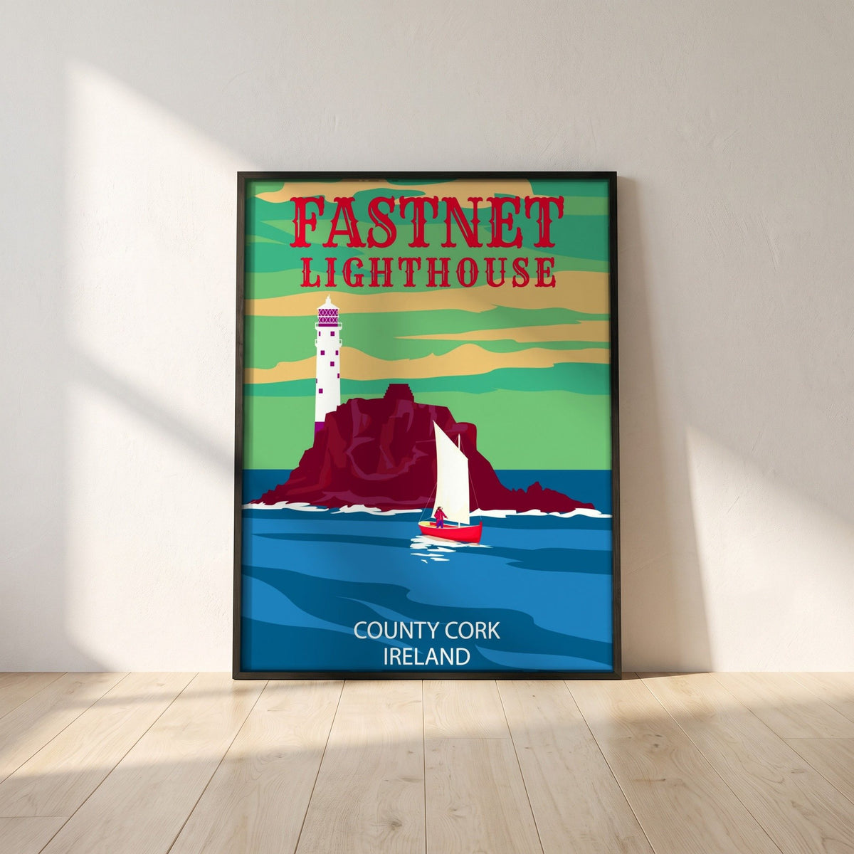 Fastnet Lighthouse retro travel poster framed print in a black frame leaning against a white plaster wall on oak floorboards in morning light