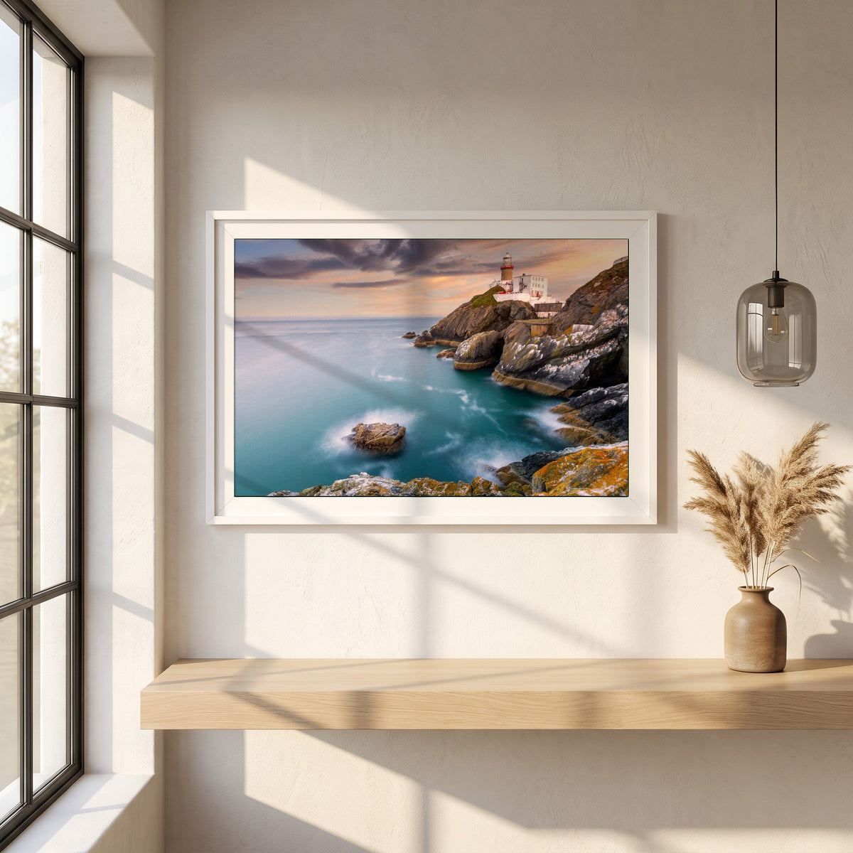 Baily Lighthouse Sunset, Howth Head framed print in a white frame on a plaster wall above an oak worktop in a bright Scandinavian kitchen
