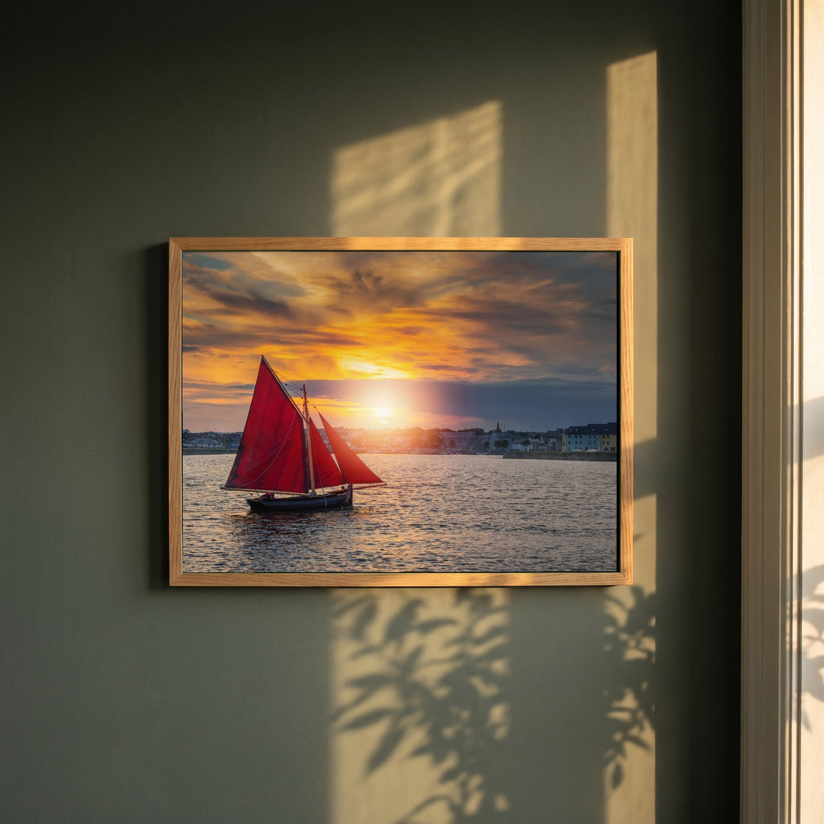 Galway Hooker framed print in a natural oak frame on a dark green wall beside a window, dappled plant shadow