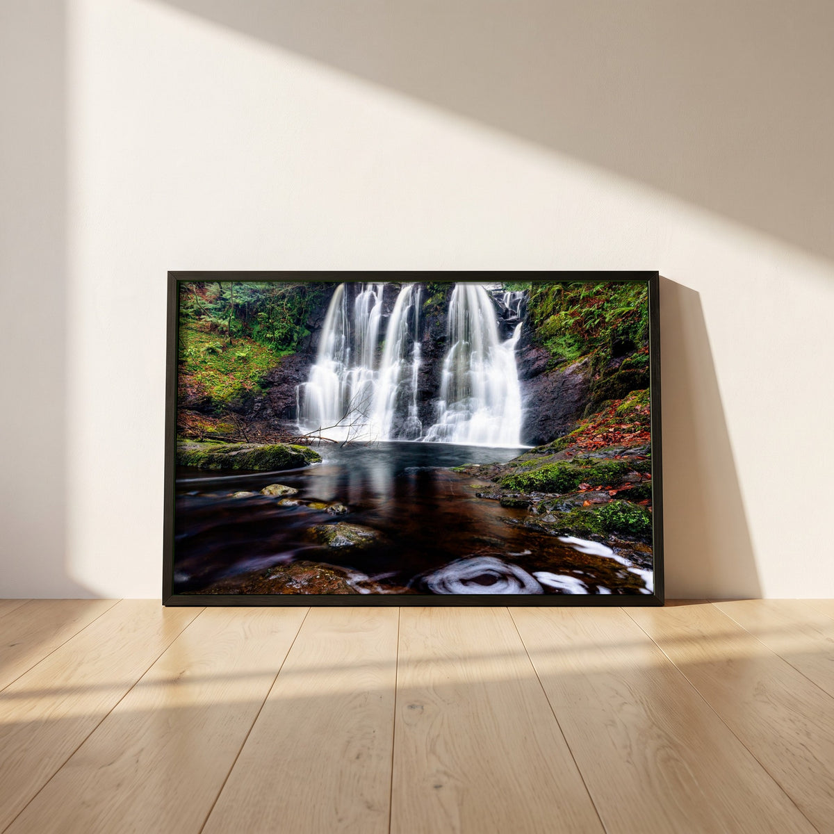 Glenariff Waterfall framed print in a black frame leaning against a white plaster wall on oak floorboards in morning light