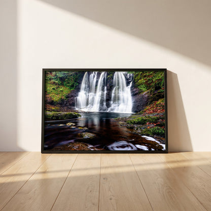 Glenariff Waterfall framed print in a black frame leaning against a white plaster wall on oak floorboards in morning light