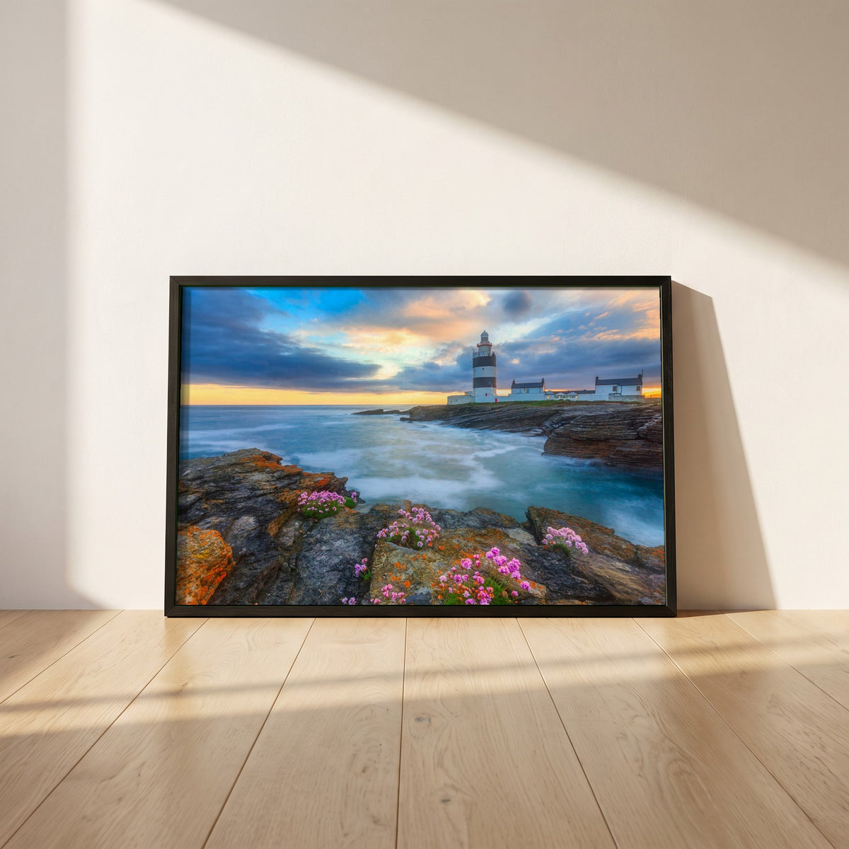 Hook Head Lighthouse, Wexford framed print in a black frame leaning against a white plaster wall on oak floorboards in morning light
