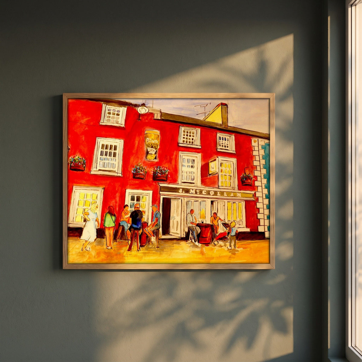 Johnny Joe's Pub, Cushendall framed print in a natural oak frame on a dark green wall beside a window, dappled plant shadow