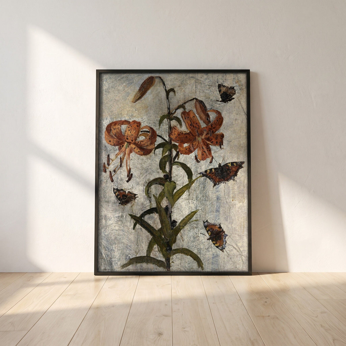 Lilies and Butterflies by Nathaniel Hone framed print in a black frame leaning against a white plaster wall on oak floorboards in morning light