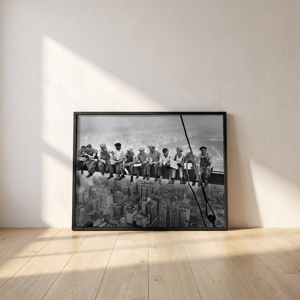 Lunch Atop a Skyscraper framed print in a black frame leaning against a white plaster wall on oak floorboards in morning light