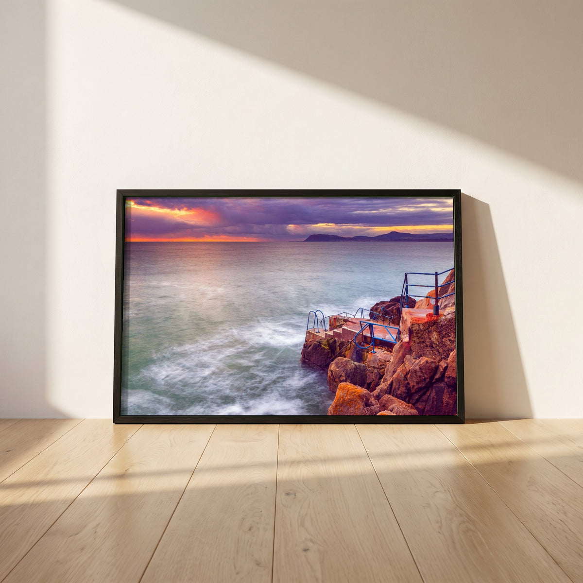 Vico Swimming Dalkey framed print in a black frame leaning against a white plaster wall on oak floorboards in morning light