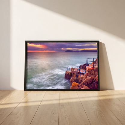 Vico Swimming Dalkey framed print in a black frame leaning against a white plaster wall on oak floorboards in morning light